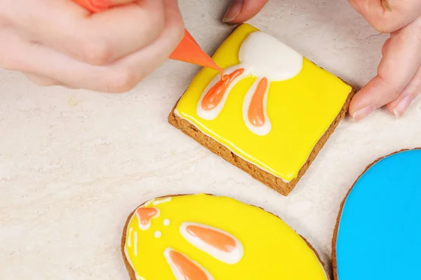 Drawing rabbit ears on a square gingerbread coated with yellow glaze