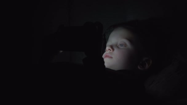 7 éves gyermek fiú használ smartphone, éjjel az ágyban — Stock videók