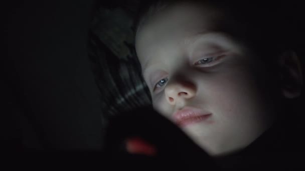 Niño de 7 años usando smartphone por la noche en la cama — Vídeo de stock