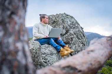 Hipster adam dizüstü bilgisayarla çalışıyor kayalık dağda oturuyor güzel manzaralı klipsli arka planda