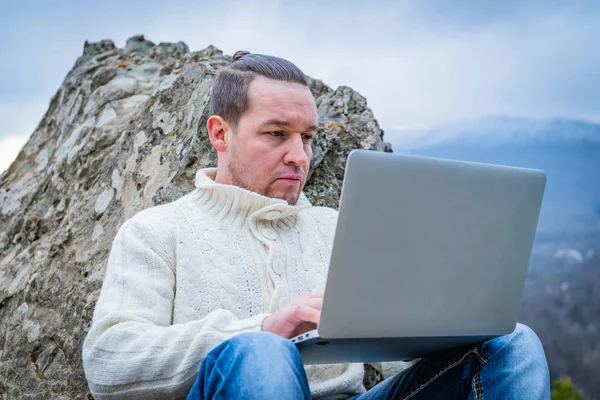 Dobrze ubrany człowiek pracujący z laptopem siedzącym na skalistej górze na pięknym, malowniczym tle klifu — Zdjęcie stockowe