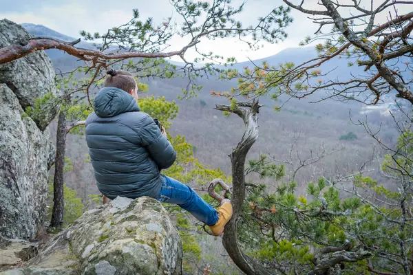 Viajero con monóculo sentado en un acantilado de montaña y mira a la distancia . — Foto de Stock