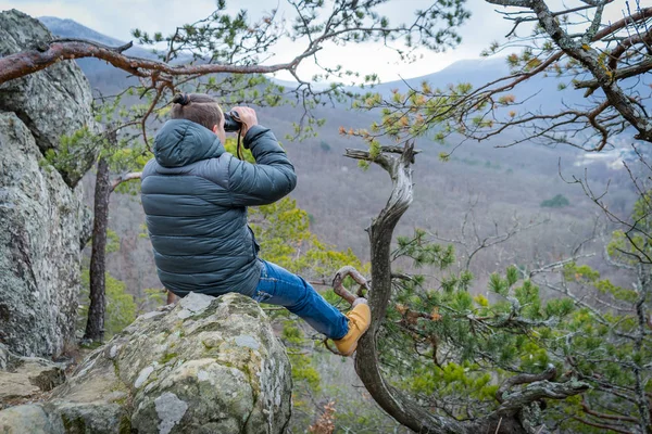 Viajero con monóculo sentado en una gran rama de conífera y mira a la distancia . — Foto de Stock
