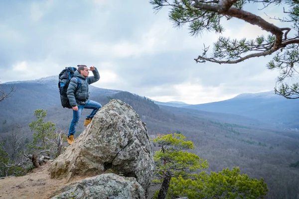 The traveler climbs to the top of the cliff and look into the distance, hiking, travel concept. — Stock Photo, Image