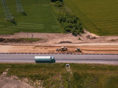 Otoyola yakın bir inşaat alanında, makineler, buldozer ve kazılar var. 4K video, yukarıdan aşağıya görünüm.