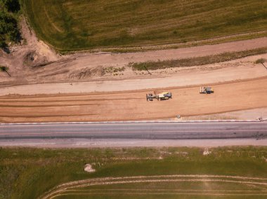 Otoyola yakın bir inşaat alanında, makineler, buldozer ve kazılar var. 4K video, yukarıdan aşağıya görünüm.