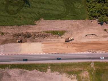 Otoyola yakın bir inşaat alanında, makineler, buldozer ve kazılar var. 4K video, yukarıdan aşağıya görünüm.