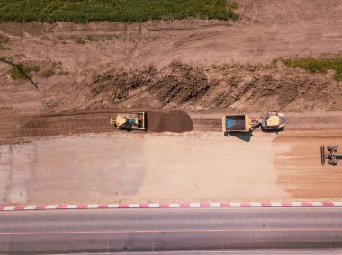 Otoyola yakın bir inşaat alanında, makineler, buldozer ve kazılar var. 4K video, yukarıdan aşağıya görünüm.