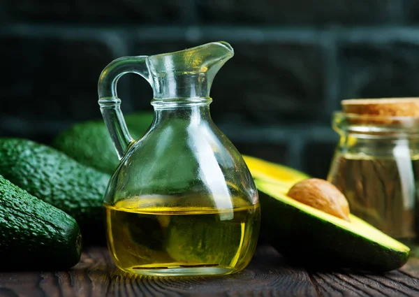 Fresh avocados and oil in glass jug — Stock Photo, Image