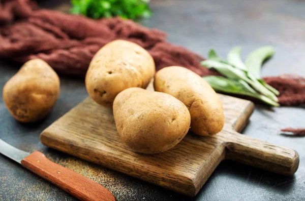 Ruwe aardappelen op een houten bord — Stockfoto