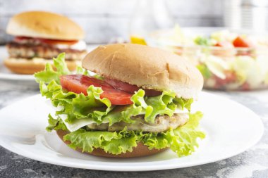 Tavuk burgeri beyaz tabakta kapanıyor. Hamburger, peynir, marul, pastırma, domates ve beyaz sos.. 