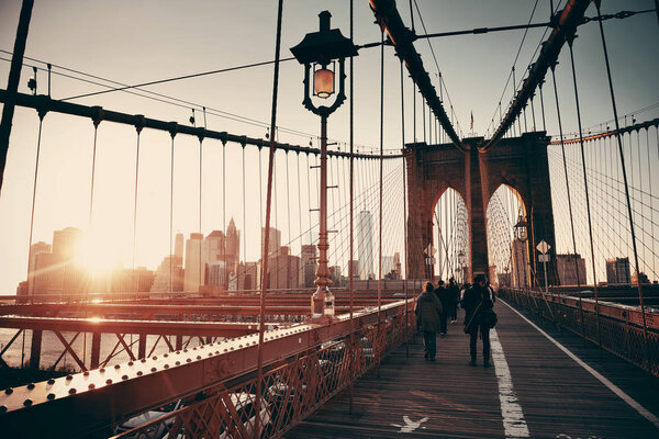 Walk on Brooklyn Bridge with pedestrians at sunset in downtown Manhattan New York City