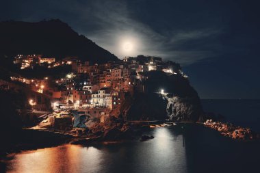 Manarola Akdeniz 'i ve Ay' ın yükselişini Cinque Terre 'deki uçurumdan gece vakti geçen binalarla gözden geçirir..