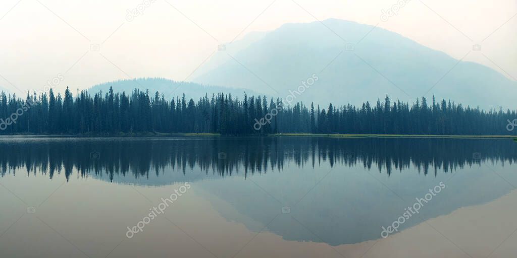 Mountain and forest over lake with reflections in a foggy day.