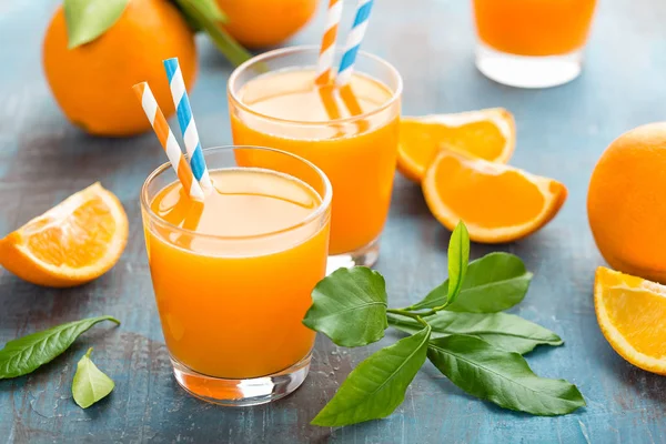 Orange juice in glass and fresh fruits with leaves on wooden background