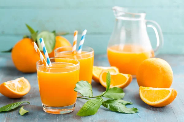 Orange juice in glass and fresh fruits with leaves on wooden background