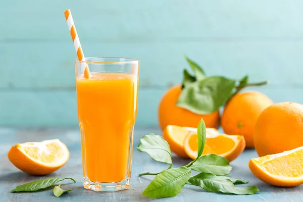 Apelsinjuice i glas och färsk frukt med lämnar på trä bakgrund — Stockfoto