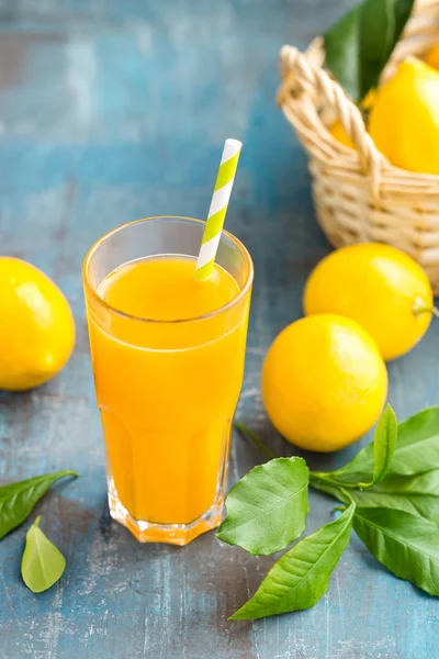 Лимонный сок в стекле и свежие фрукты с листьями на деревянном фоне — стоковое фото