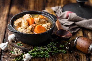 Meat stewed with carrots in sauce and spices in cast iron pot on dark wooden rustic background clipart