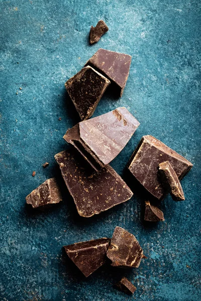 Trozos de chocolate negro aplastados sobre un fondo oscuro, vista desde arriba — Foto de Stock