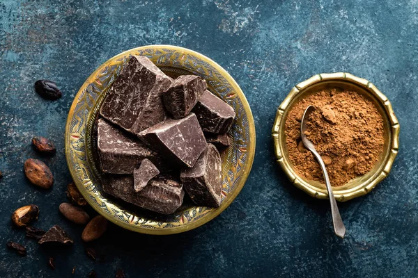 Dunkle Schokoladenstücke zerkleinert und Kakaobohnen, kulinarischer Hintergrund, Draufsicht — Stockfoto