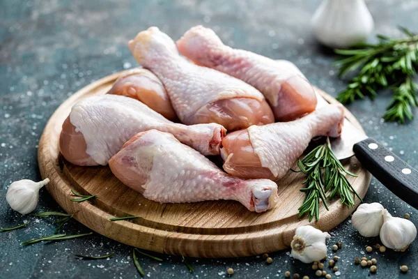 Pernas de frango crus não cozidas, baquetas na tábua de madeira, carne com ingredientes para cozinhar — Fotografia de Stock