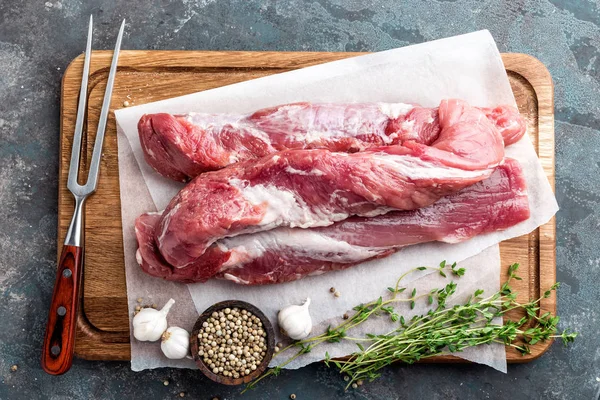 Fresh raw pork tenderloin on wooden cutting board on dark background — Stock Photo, Image