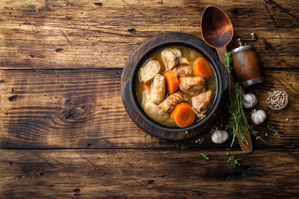 Vlees gestoofd met wortelen in de saus en kruiden in gietijzeren pot op donkere houten rustieke achtergrond — Stockfoto