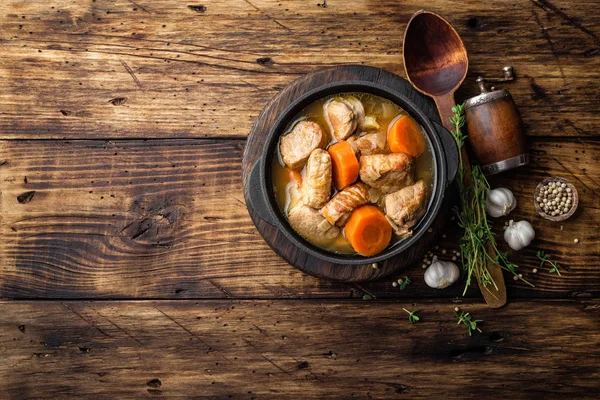 Carne estofada con zanahorias en salsa y especias en maceta de hierro fundido sobre fondo rústico de madera oscura —  Fotos de Stock