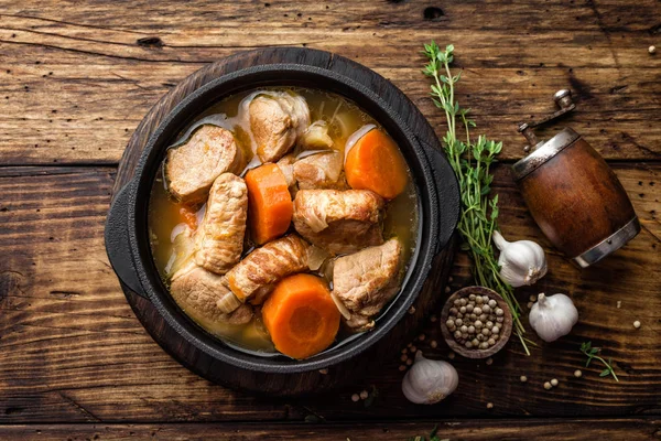 Meat stewed with carrots in sauce and spices in cast iron pot on dark wooden rustic background