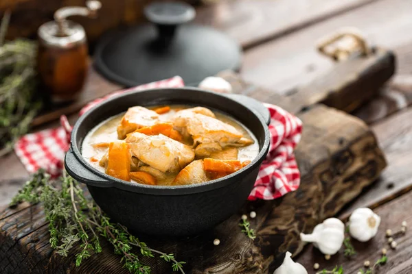 Viande cuite avec des carottes en sauce et épices dans une casserole en fonte sur fond rustique en bois foncé — Photo