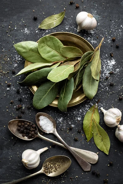 Dunkler kulinarischer Hintergrund mit Lorbeer, Salz, Pfeffer und Knoblauch — Stockfoto