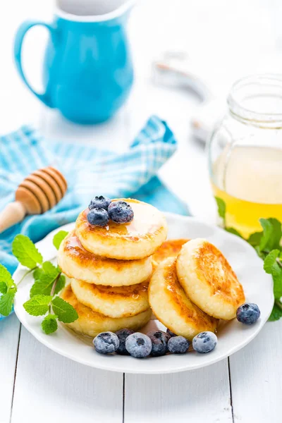 Сирні млинці з медом та чорницею на білому тлі, сніданок або обід — стокове фото