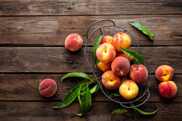 Fresh peaches fruits with leaves in basket on dark wooden rustic background, top view — Stock Photo, Image