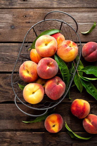 Fresh peaches fruits with leaves in basket on dark wooden rustic background, top view — Stock Photo, Image