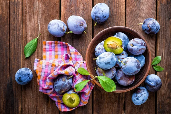 Fresh plums with green leaves on wooden rustic background, top view — Stock Photo, Image