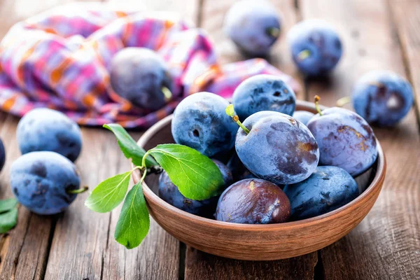 Fresh plums with green leaves on wooden rustic background — Stock Photo, Image