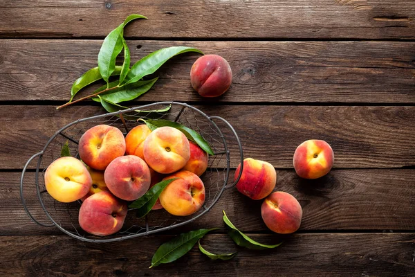 Fresh peaches fruits with leaves in basket on dark wooden rustic background, top view — Stock Photo, Image