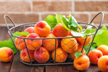 Ahşap masa üzerinde sepet içinde yapraklarla taze kayısı