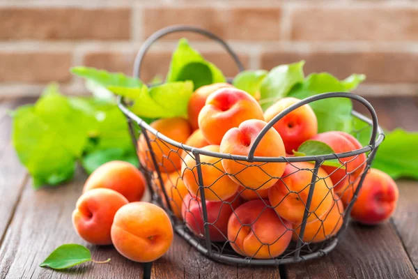 Fresh apricots with leaves in basket on wooden table — Stock Photo, Image