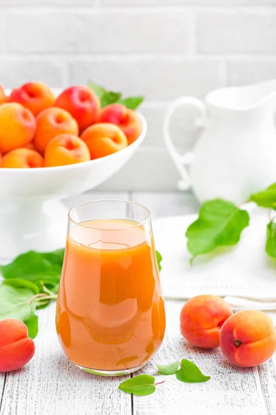 Aprikos juice och färsk frukt med blad på vit trä bord — Stockfoto