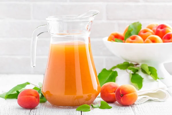 Apricot juice and fresh fruits with leaves on white wooden table — Stock Photo, Image