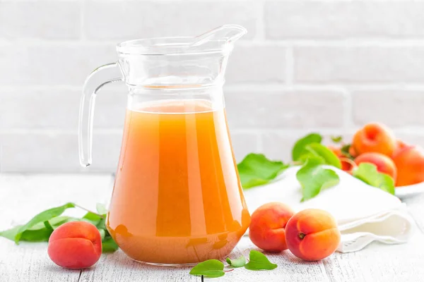 Jus d'abricot et fruits frais avec feuilles sur table en bois blanc — Photo