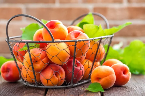 Fresh apricots with leaves in basket on wooden table — Stock Photo, Image