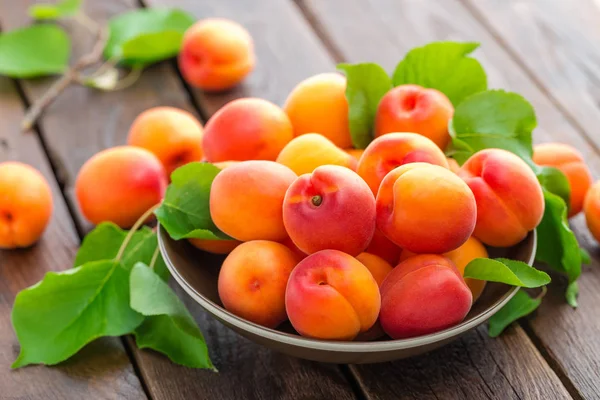 Fresh apricots with leaves on wooden table — Stock Photo, Image