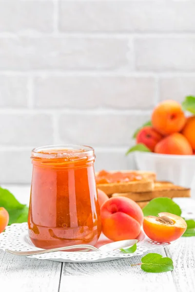 Marillenmarmelade im Glas und frische Früchte mit Blättern auf weißem Holztisch, Frühstück — Stockfoto