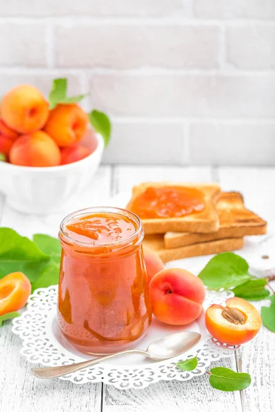 Marillenmarmelade im Glas und frische Früchte mit Blättern auf weißem Holztisch, Frühstück — Stockfoto