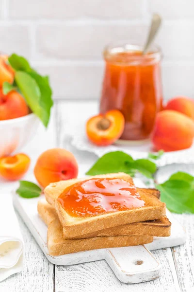 Tostadas de pan con mermelada de albaricoque y fruta fresca con hojas sobre mesa de madera blanca. Sabroso desayuno . —  Fotos de Stock