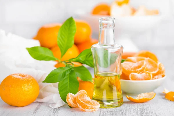 Tangerinas com folhas e garrafa de óleo cítrico essencial sobre um fundo branco — Fotografia de Stock