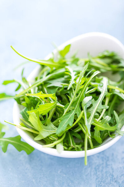 Fresh arugula leaves in bowl on table. Light background, closeup